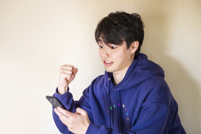 スマホを見て喜ぶ男性の写真